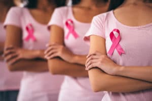 3 women wearing pink, stand with their arms folded sporting the pink Breast Cancer Awareness ribbon
