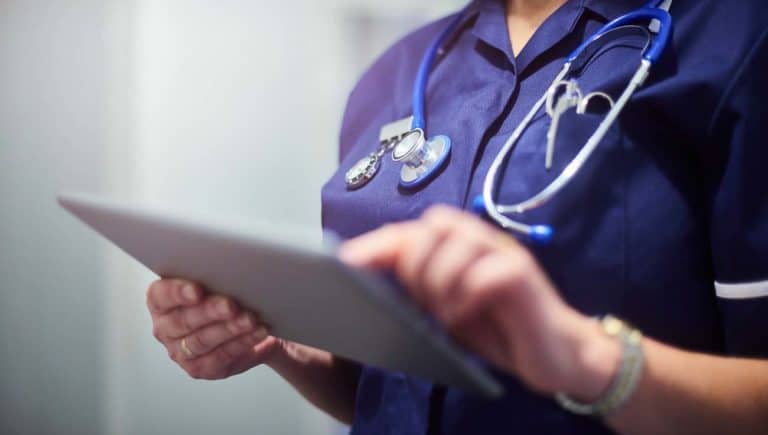 Nurse wearing blue uniform and stethoscope uses tablet