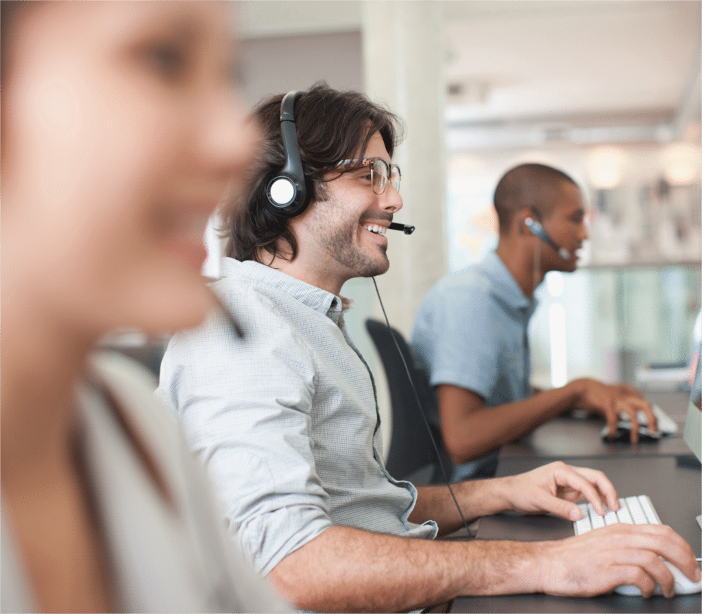 Office workers speak into headsets whilst smiling at their computer screens