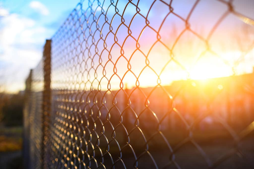 A metal prison fence is in the foregournd with a beautiful sunset behind the fence in the distance.